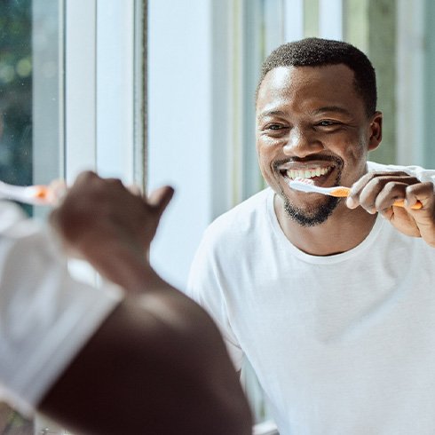Man smiling while brushing his teeth in bathroom