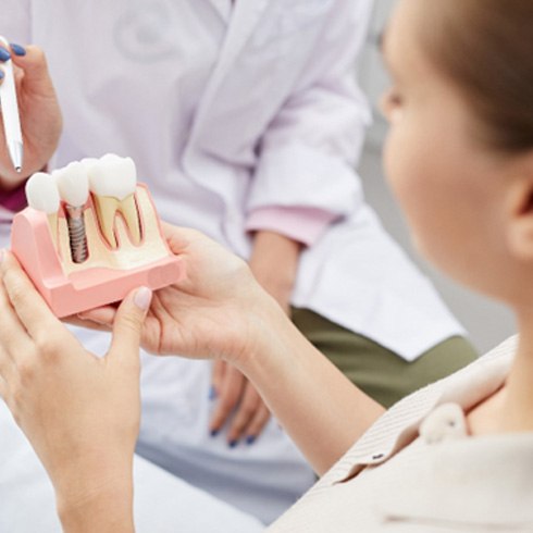 Female patient looking at a model of a dental implant in Jersey City, NJ