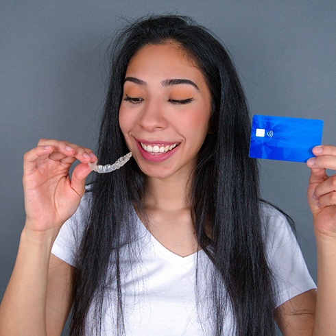 A woman holding a clear aligner in one hand and a credit card in the other