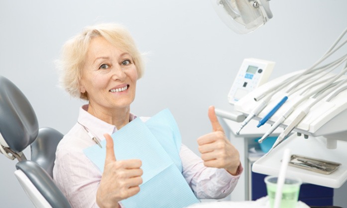 Older dental patient giving a thumbs up for her dentures