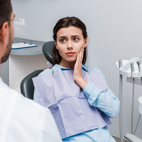 Woman with toothache looking at dentist while holding her cheek