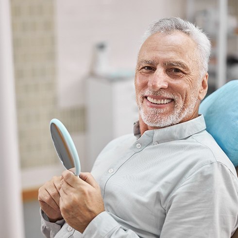 Bearded man smiling in dental chair with mirror