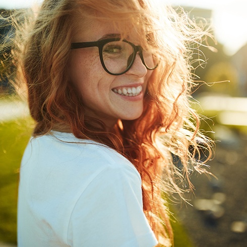 Red-haired woman with glasses outside and smiling