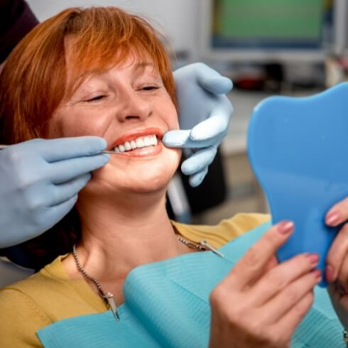 Woman looking at smile in a mirror after dental implant tooth replacement