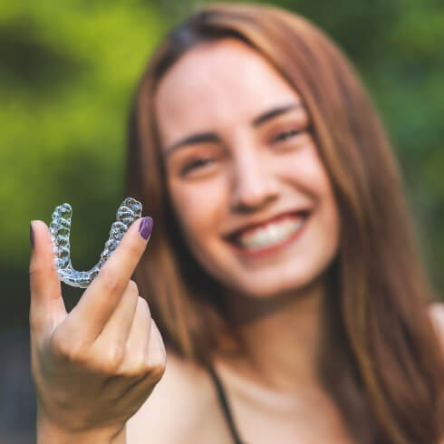 Woman holding up a clear correct aligner tray