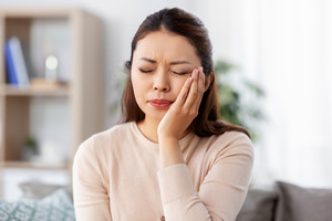 Woman with infected tooth rubbing cheek in pain